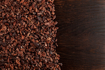 Cocoa nibs on brown wooden surface, close-up. Design element, copy space. Cocoa nibs are usually used to make a hot drink that tastes like hot chocolate. Sugar-free product,  Natural antidepressant