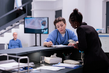 African american reception worker checking medical report with assistant discussing patient expertise while working at medication treatment during checkup visit in hospital lobby. Medicine concept