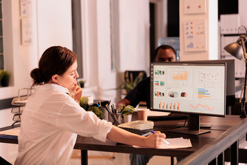 Company analyst analyzing marketing report diagrams on computer screen, employee working on company research statistics in coworking space. Woman checking dashboard in office with sunset light