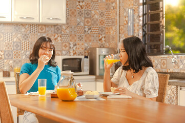 Two young asian ladies having breakfast at the kitchen with orange juice and cheese breads. (Pao de queijo)