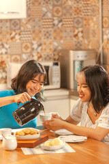 Asian young lady serving coffee on breakfast to her sister at the kitchen.