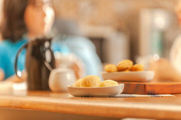 Cheese breads on the table with girls having breakfast behind. (Pao de queijo)