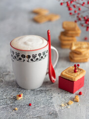  Cup of coffee with milk on the gray background, biscuits, red decorations, sweet Italian/Mediterranean breakfast.