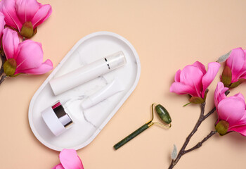 White plastic tub, jar on a marble stand, and a bouquet of pink magnolia, top view.