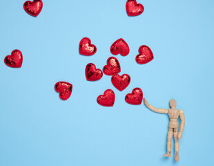 Wooden mannequin toy and red hearts on a blue background, concept of love