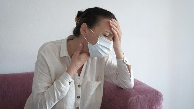 Sick woman with sore throat in mask indoor. An ill female suffer from sora throat and wear protective mask in the room.