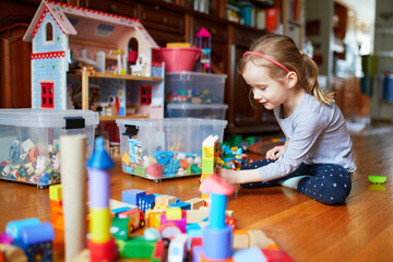 Adorable prechooler girl sitting on the floor and playing with colorful construction blocks