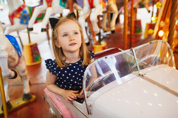 Adorable preschooler girl in car on traditional Parisian vintage merry-go-round in Paris