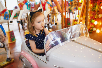 Adorable preschooler girl in car on traditional Parisian vintage merry-go-round in Paris