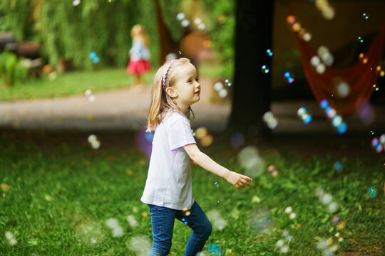 Happy adorable preschooler girl playing with bubbles outdoors on a summer day