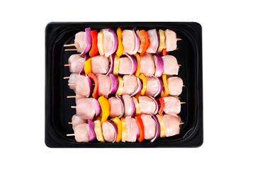 Raw chicken skewers of fillet with vegetables, pineapple, peppers, onions, in a tray on a white background. Skewers with pieces of raw meat, red, yellow and green pepper.Close-up.Top view.