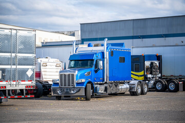 Cluster of big rigs semi trucks tractors and semi trailers standing on the warehouse parking lot in...