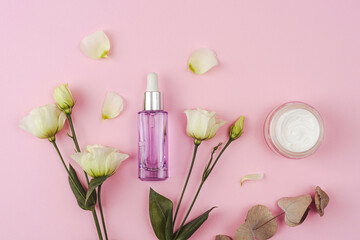 Purple cosmetic bottle, cream jar, white eustoma flowers and eucalyptus leaves on pink background. Top view, flat lay