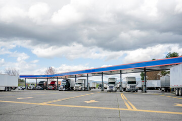 Row of the big rigs semi trucks with loaded semi trailers standing on the fuel station on the truck...
