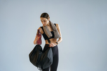 Woman with sports bag and bottle of water after training on studio background. High quality photo