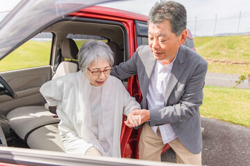 自動車から降りて車椅子に乗る高齢者女性と介助する男性（移乗）
