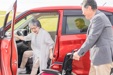 自動車から降りて車椅子に乗る高齢者女性と介助する男性（移乗）
