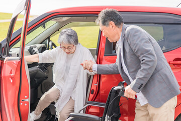 自動車から降りて車椅子に乗る高齢者女性と介助する男性（移乗）
