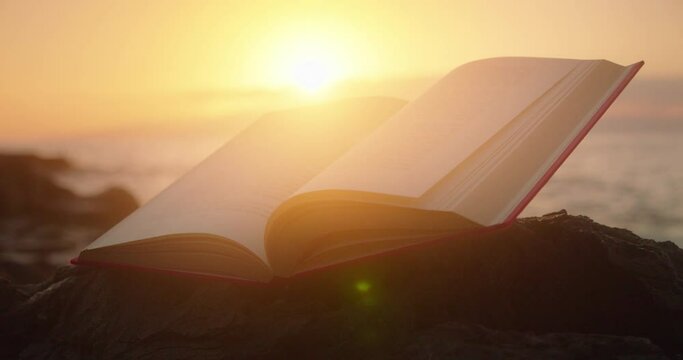 Enchanted magic open book on rocky beach at sunset glow light.