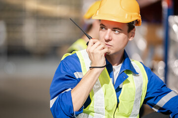 Happy Professional man Manager Worker Wearing Safety Vest and Hard Hat Smiling on Camera. In the Background Big Warehouse with Shelves full of Delivery Goods.