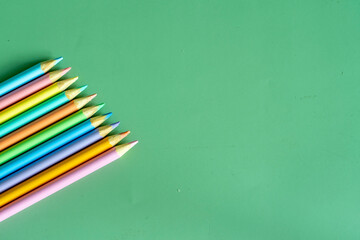 Pastel colored pencils, top view on green background, illustration concept, education and back to school