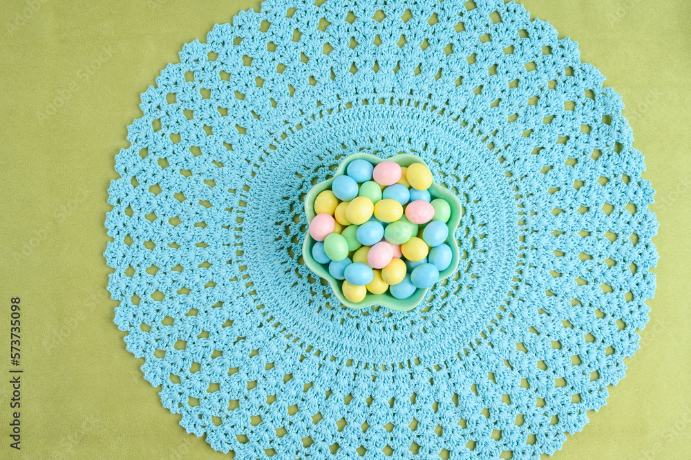 Wall mural Bowl of candy coated easter eggs on a pastel blue lace placemat
