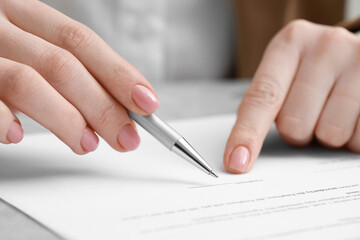 Woman signing document at light grey marble table, closeup