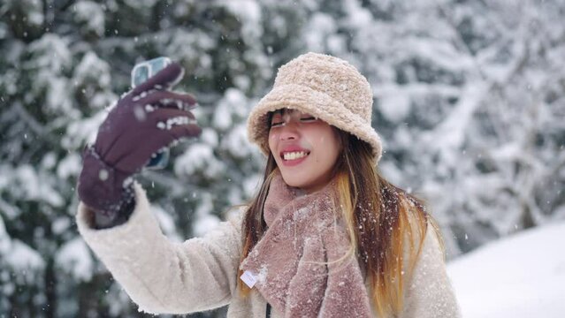 Asian woman in winter coat vlogging on mobile phone during walking on footpath on forest mountain in snow day. Attractive girl travel local village covered in snow in Japan on winter holiday vacation.