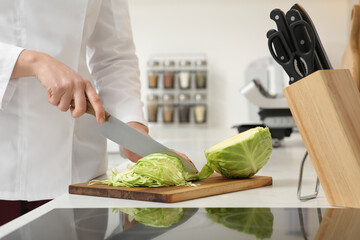 Professional chef cutting cabbage at white countertop in kitchen, closeup