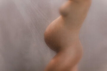 Pregnant woman in shower showing belly bump naked out of focus blurred beautiful body during...
