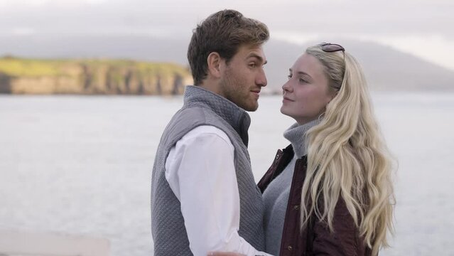 Happy Preppy Romantic Young White Couple during Sunset Golden Hour by the Ocean - looking out at water and turning back