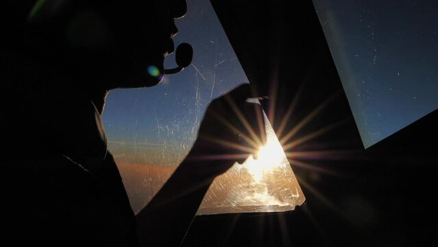 Close up of a male pilot in airplane´s cockpit speaking on radio in slow motion backlit by the setting sun
