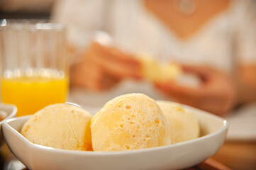 Cheese breads on the table with a girl having breakfast behind. (Pao de queijo)