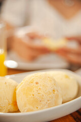 Cheese breads on the table with a girl having breakfast behind. (Pao de queijo)