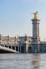 Fototapeta na wymiar Alexandre III bridge against hazy blue sky with river Seine in the foreground in Paris, France