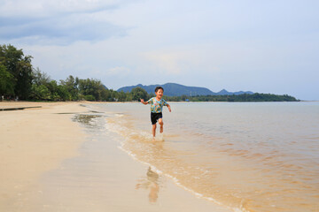 Happy Asian little boy having fun running on tropical sand beach