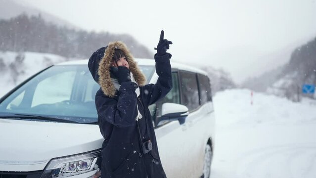 Upset Asian Woman Standing Outside The Car Using Mobile Phone Calling For Assistance While Her Vehicle Breakdown Or Run Out Of Gas On Roadside In Snow Day. Car Insurance And Automobile Problem Concept