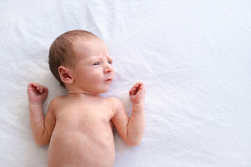 Close up of caucasian hairy brunet cute newborn baby lying on back on white sheet.Naked one week old child, half body shot, copy space for text.High angle, top view.