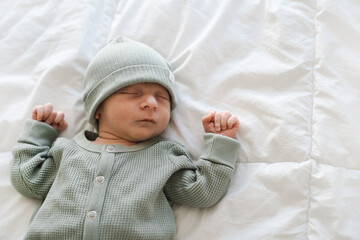 Half body shot of caucasian hairy brunet cute newborn baby sleeping wearing green crawlers and cap.One or two week old, few days child.Copy space.