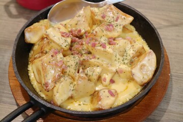 Baked cheese potato cubes and ham slices in an iron plate