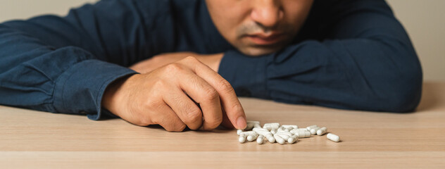 Stressed, sad asian young man, male holding medicine, lying on table. Close up hand of abuse overdose pills and addict. Sick pain of health treatment, unhappy people. Suicide depressed or despair.