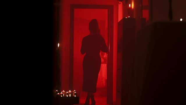silhouette of a woman at the end of a corridor in a dark environment with red light and candles