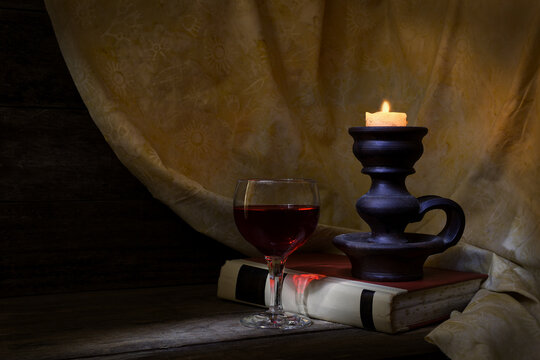 Classic, Still Life setting, red wine, glass, old book, lit candle in soft, warm, mood lighting, shaft of light coming from the left