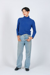 Portrait isolated cutout studio full body shot of Asian young gay male model in turtleneck longsleeve shirt denim jeans with high heel leather shoes standing posing look at camera on white background