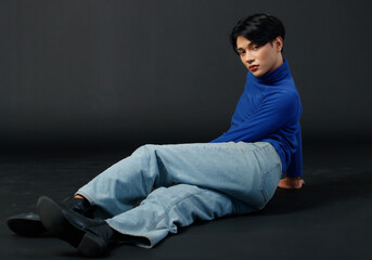 Portrait studio closeup shot of Asian young sexy luxury glamour slim fashionable LGBTQ gay male model in turtleneck long sleeve shirt jeans leather boots sitting sleek hair posing on black background