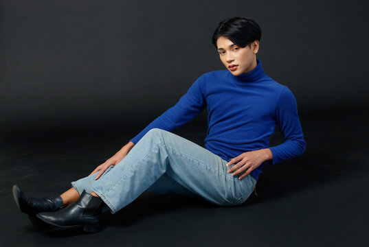 Portrait Studio Closeup Full Body Shot Of Asian Young Sexy Luxury Glamour Slim Fashionable LGBTQ Gay Male Model In Turtleneck Long Sleeve Shirt Jeans Sitting Holding Leg Up Posing On Black Background