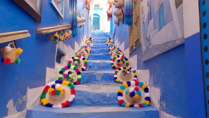 Climbing Pov Picturesque staircase with a colorful straw hats on the blue walls, Chefchaouen