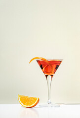 Martinez alcoholic cocktail drink with red vermouth, liqueur, orange bitter, zest and ice. Light beige background, hard light, shadow pattern, minimalism - obrazy, fototapety, plakaty