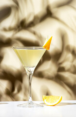 Vesper, classic alcoholic cocktail drink with dry gin, vodka, aperitif, lemon zest and ice. Light beige background, hard light, shadow pattern