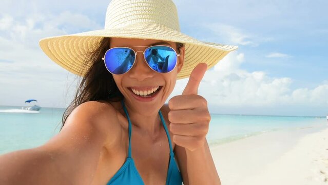 Selfie summer beach vacation travel woman taking selfie photo video with phone on beach holidays. Woman wearing beach hat and mirror sunglasses, blue swimsuit. 59.94 FPS
